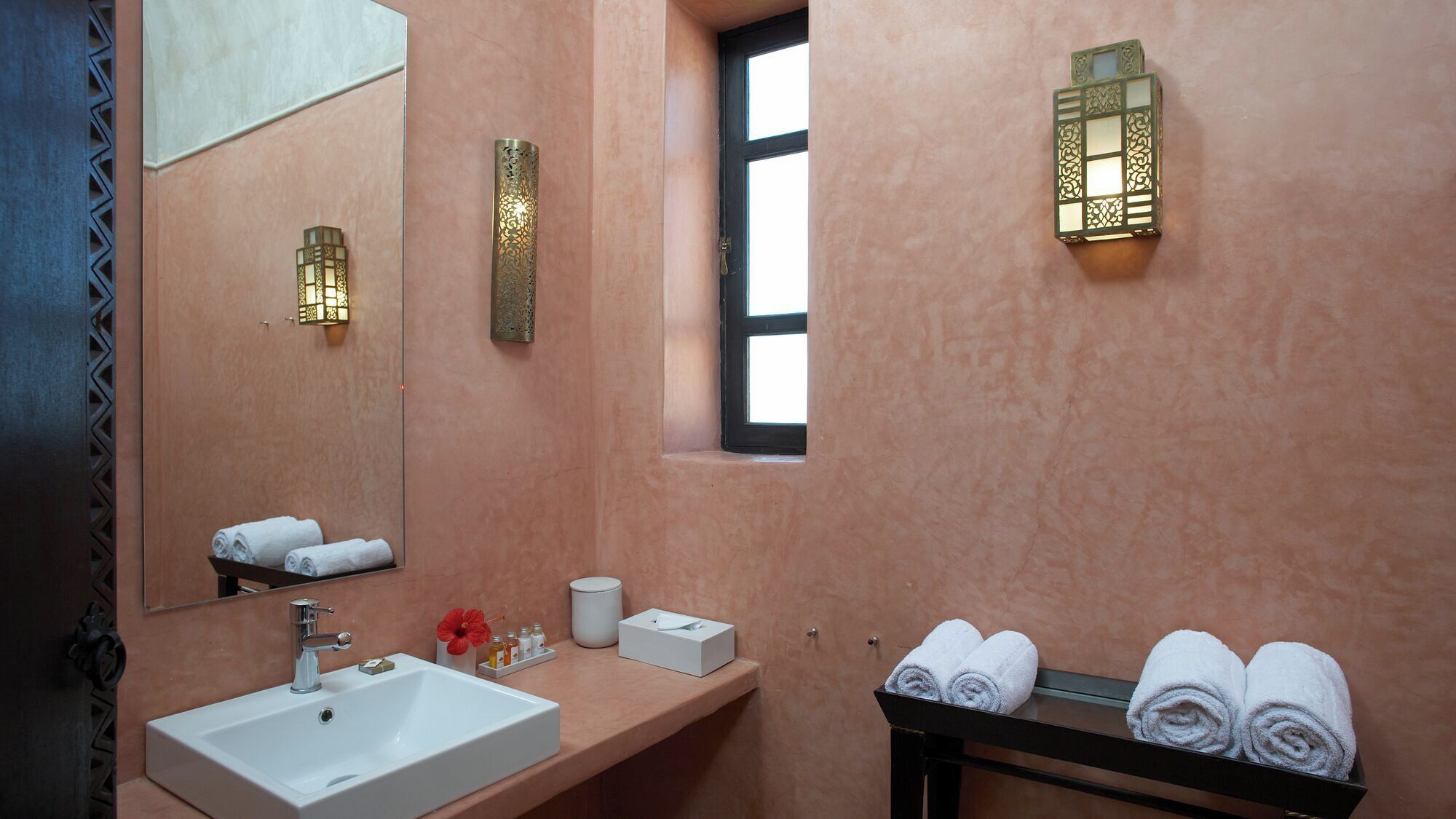 Un baño con lavamanos, espejo, toallero y apliques decorativos.