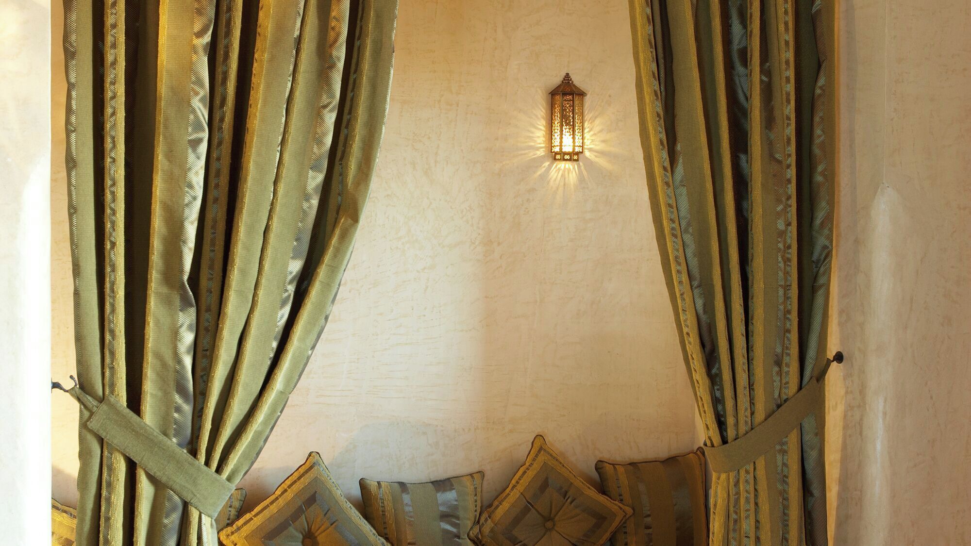 Quarto com cortinas grossas, luminária fixada na parede e cama com roupa de cama estampada.