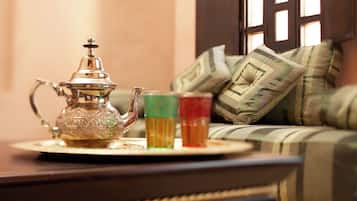 A traditional tea set with a teapot and glasses on a tray, placed on a table in a room with a sofa and pillows in the background.