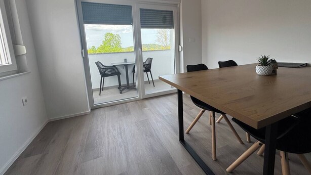 Un'elegante sala da pranzo con tavolo in legno, sedie nere e una porta scorrevole in vetro che dà su un balcone.