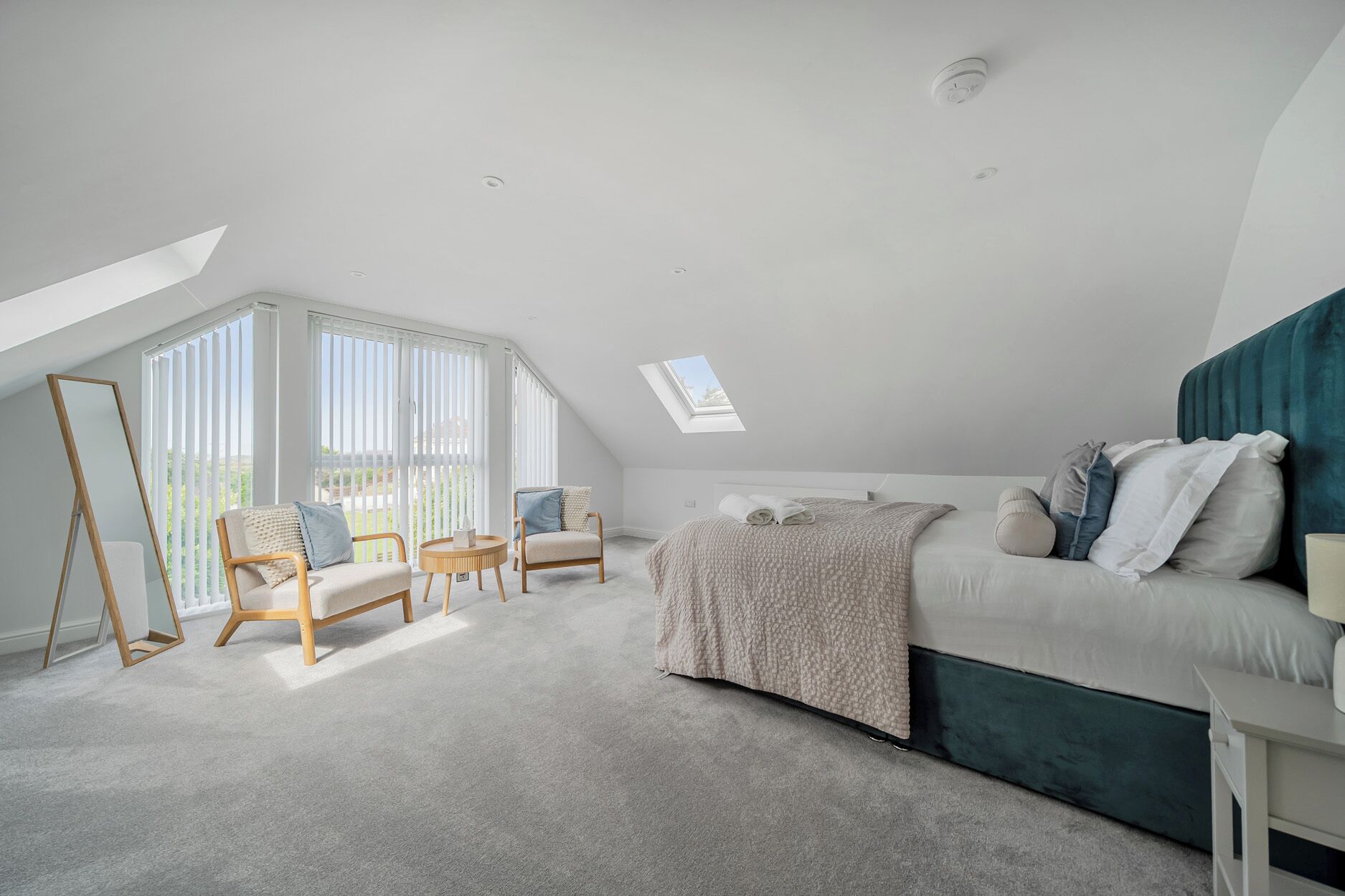 A bedroom with a sloped ceiling, a bed, a sofa, two chairs, a round table, and a skylight.