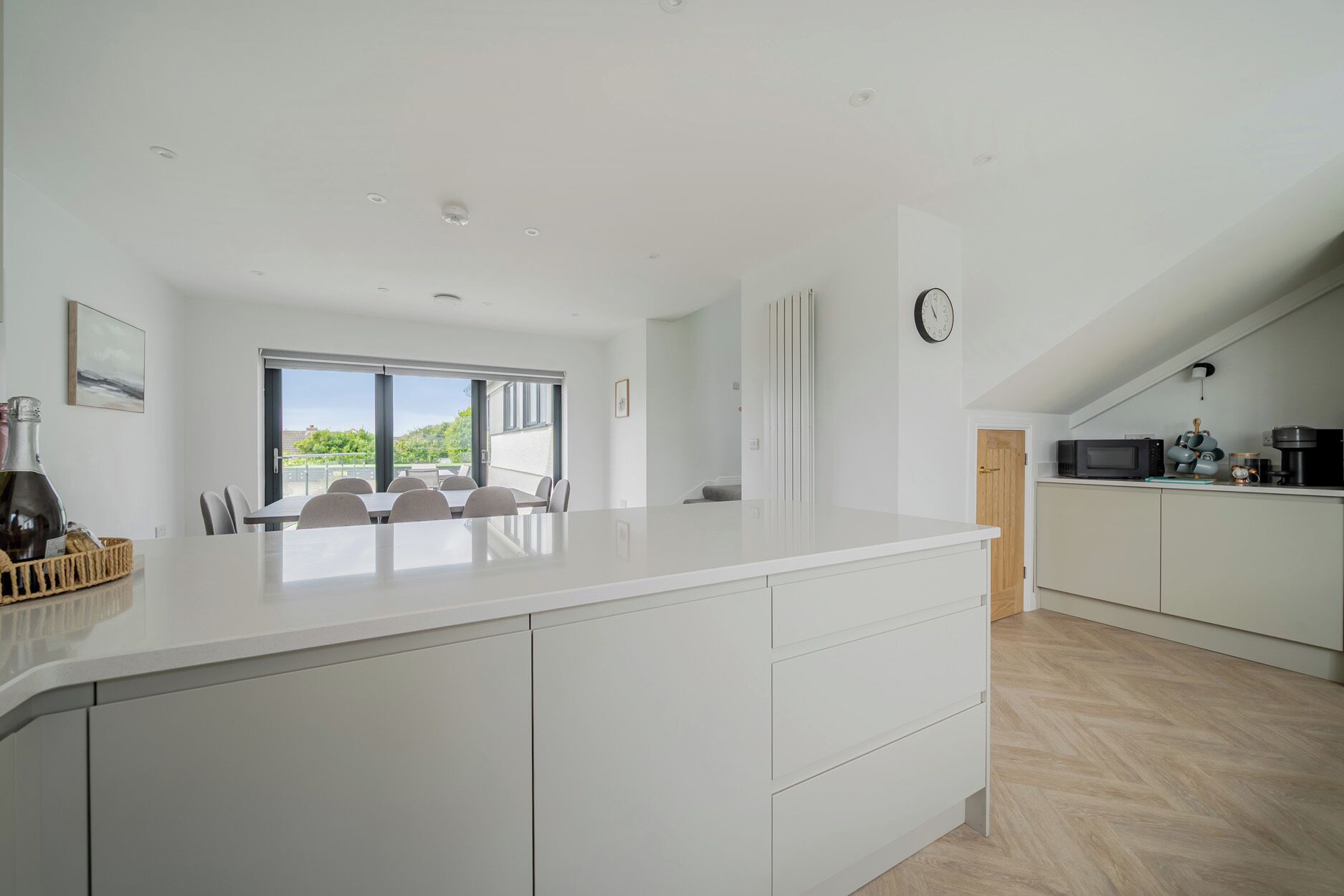 A modern kitchen with a large island, a dining area with a view, and a clock on the wall.