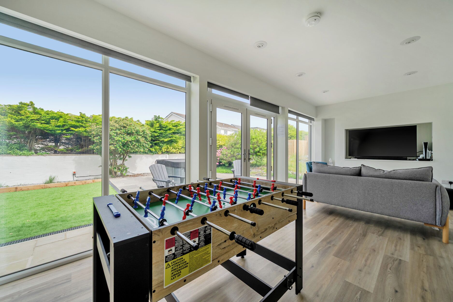 A modern living room with a foosball table, a grey sofa, and a TV mounted on the wall.