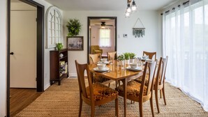 A dining area with a wooden table, chairs, and a rug. There is a bookshelf, a plant, and a ceiling fan. - Nature-Quiet Retreat • Firepit + BBQ • PetFriendly (McArthur)
