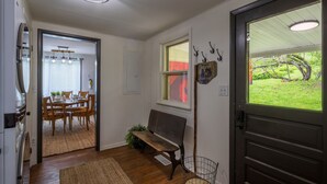 A hallway with a dining area, a bench, a door with a view, and a ceiling light fixture. - Nature-Quiet Retreat • Firepit + BBQ • PetFriendly (McArthur)