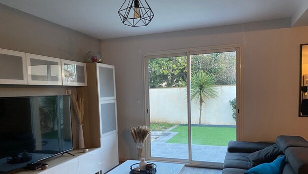Ein modernes Wohnzimmer mit einem Flachbildfernseher, einem Couchtisch, einer Couch und einer Glastür, die zu einem Garten führt.