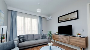 A modern living room with a grey sofa, a round coffee table, a TV on a wooden cabinet, and a large window with sheer curtains. - LUX RESIDENCE 2 ROOMS 1 SALOON (Istanbul)
