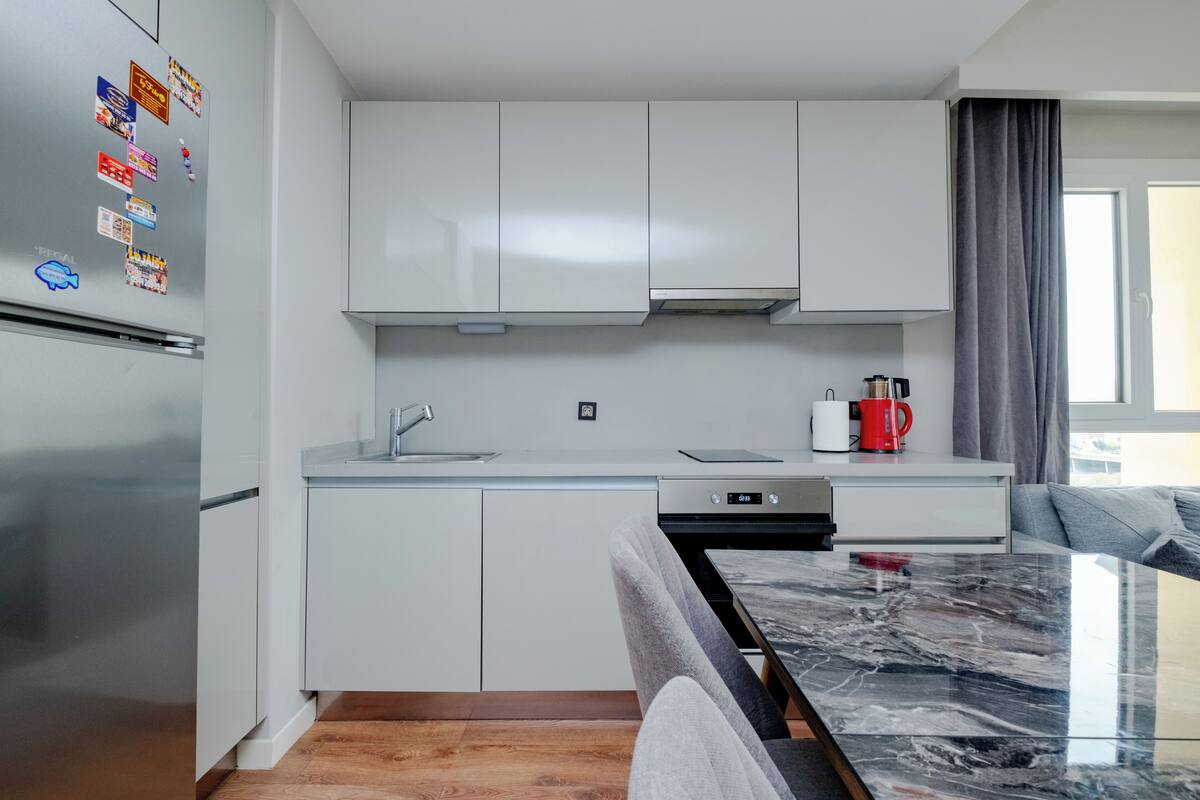 A modern kitchen with white cabinets, a stainless steel refrigerator, a coffee maker, and a marble countertop.