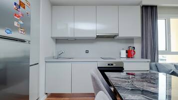 Une cuisine moderne avec des meubles blancs, un réfrigérateur en acier inoxydable, une machine à café et un plan de travail en marbre.