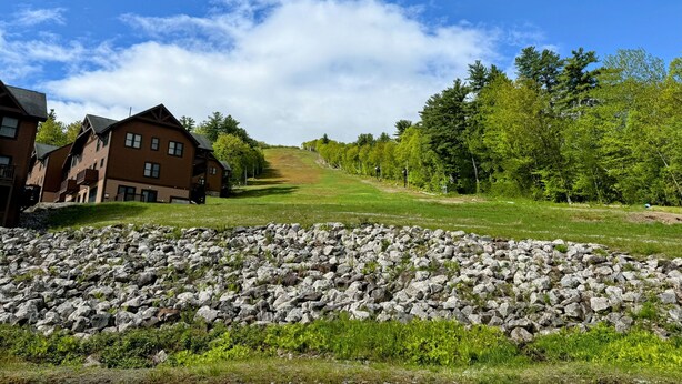 A row of wooden buildings with a stone wall in the foreground. - Cozy Lake Region Townhome – Steps from Moose Pond in Bridgton (Bridgton)