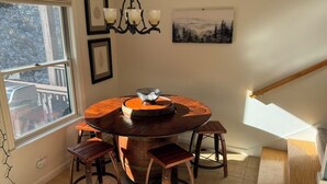 A round wooden dining table with a metal bowl centerpiece, surrounded by four wooden stools. - Cozy Lake Region Townhome – Steps from Moose Pond in Bridgton (Bridgton)