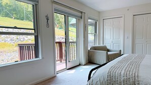 A bedroom with a large bed, a sliding glass door to a deck, and a view of a grassy area. - Cozy Lake Region Townhome – Steps from Moose Pond in Bridgton (Bridgton)