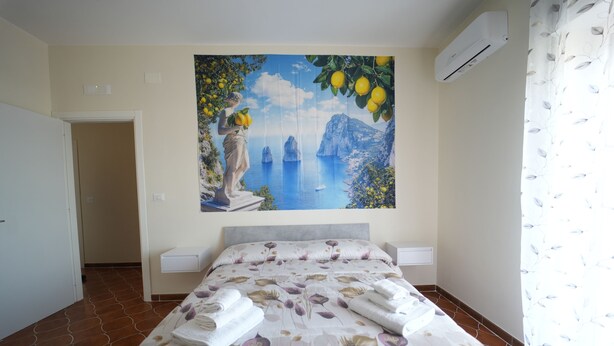 Une chambre à coucher comprenant un lit, une table de chevet, un climatiseur fixé au mur et une porte donnant sur une autre pièce.