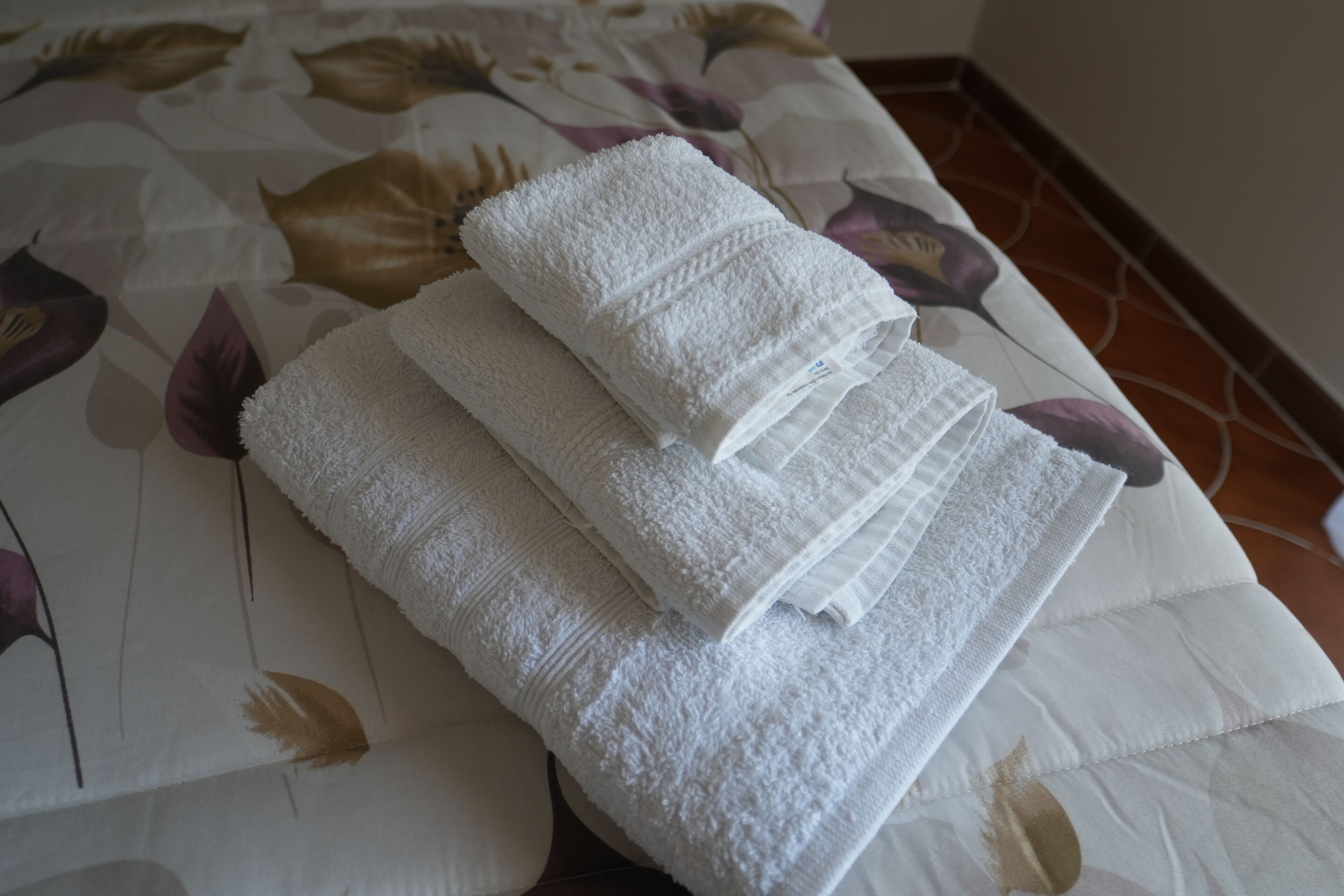 Une pile de serviettes blanches, soigneusement pliées, est posée sur un lit recouvert d’une couvre-lit à motifs floraux.