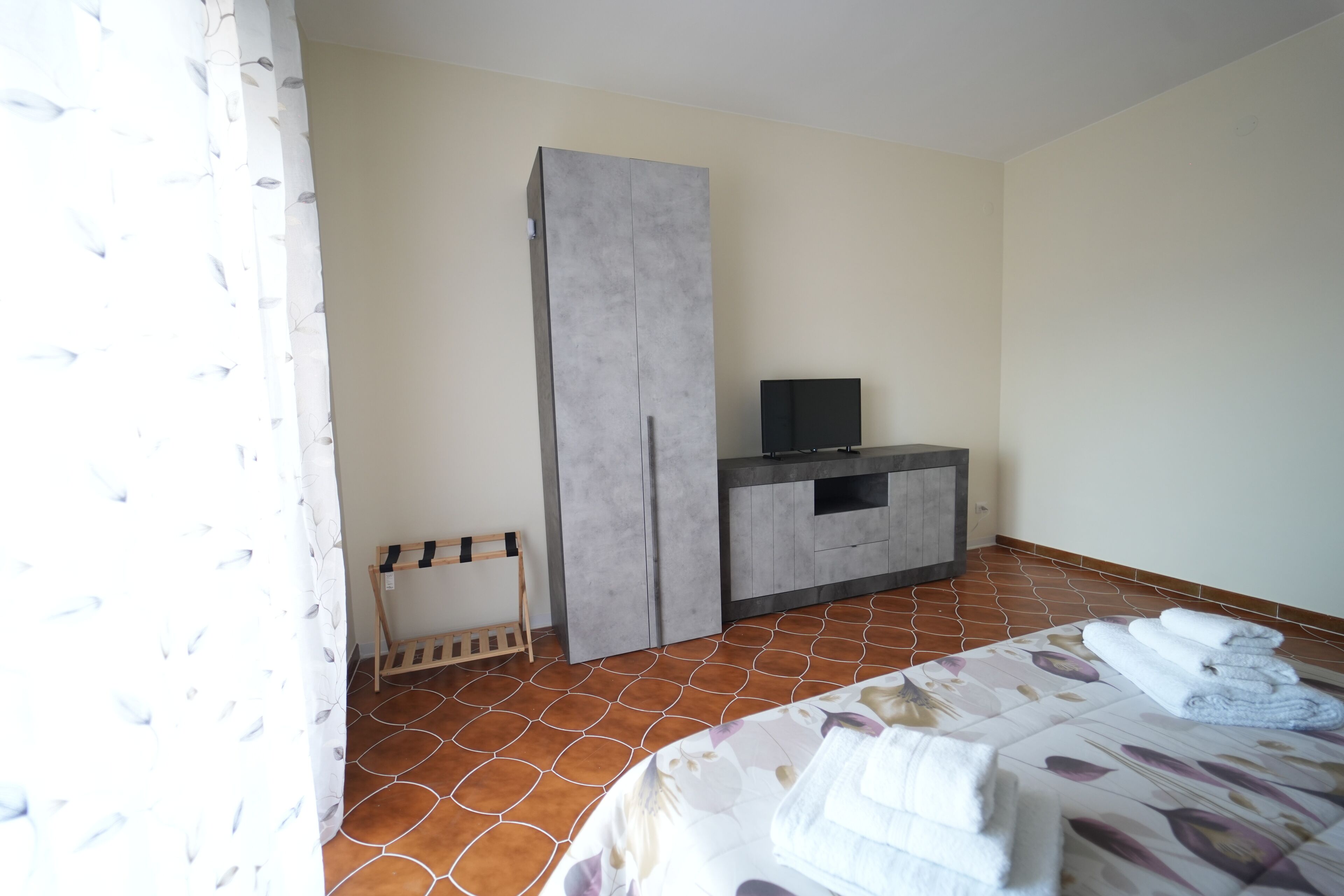 Una camera d'albergo con un letto, una televisione, un armadio e un piccolo angolo salotto.
