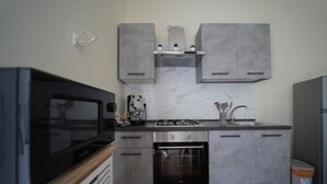 Une cuisine compacte avec des meubles gris, un four encastré, une cuisinière à gaz et un four à micro-ondes.