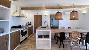 Una cocina moderna con vigas de madera, una isla central y un comedor con sillas de mimbre.