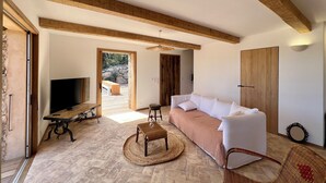 Una sala moderna con techo de madera, un sofá, un televisor y piso de piedra.