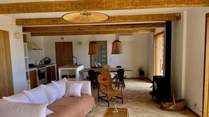 Un espacio de sala acogedor con un sofá, una mesa de comedor con sillas, una cocina al fondo y un ventanal grande.