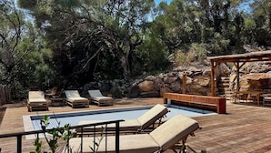 Una terraza de madera con piscina, sillas de descanso y un pérgola de madera.