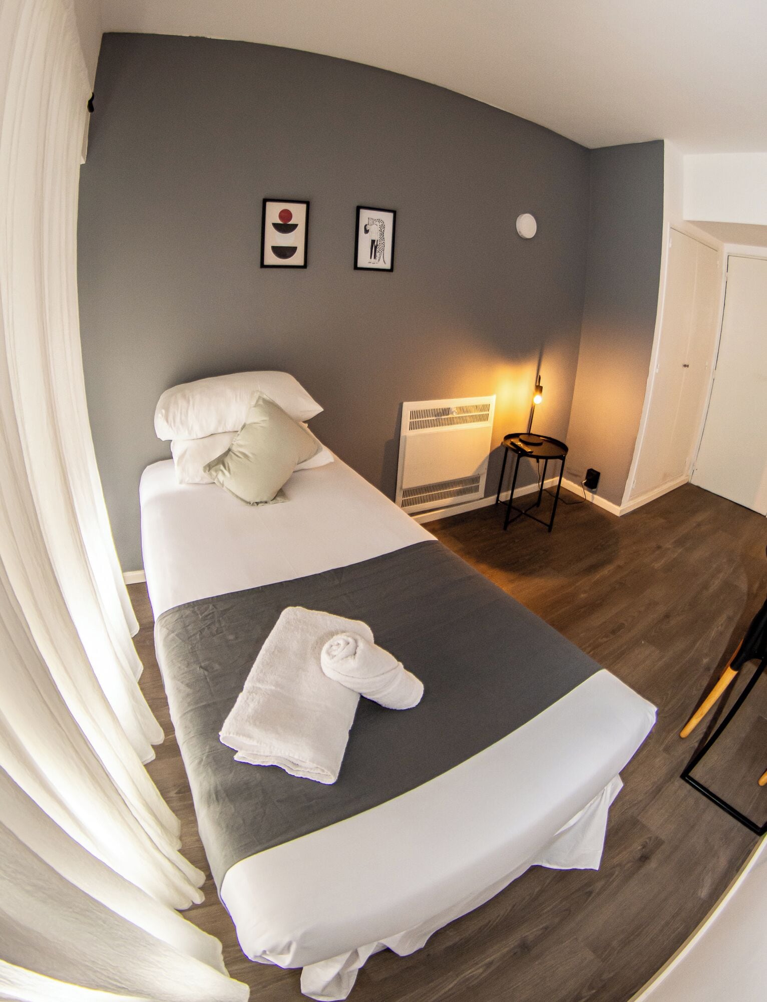 A bedroom with a bed, a bedside table, a lamp, and two framed pictures on the wall.