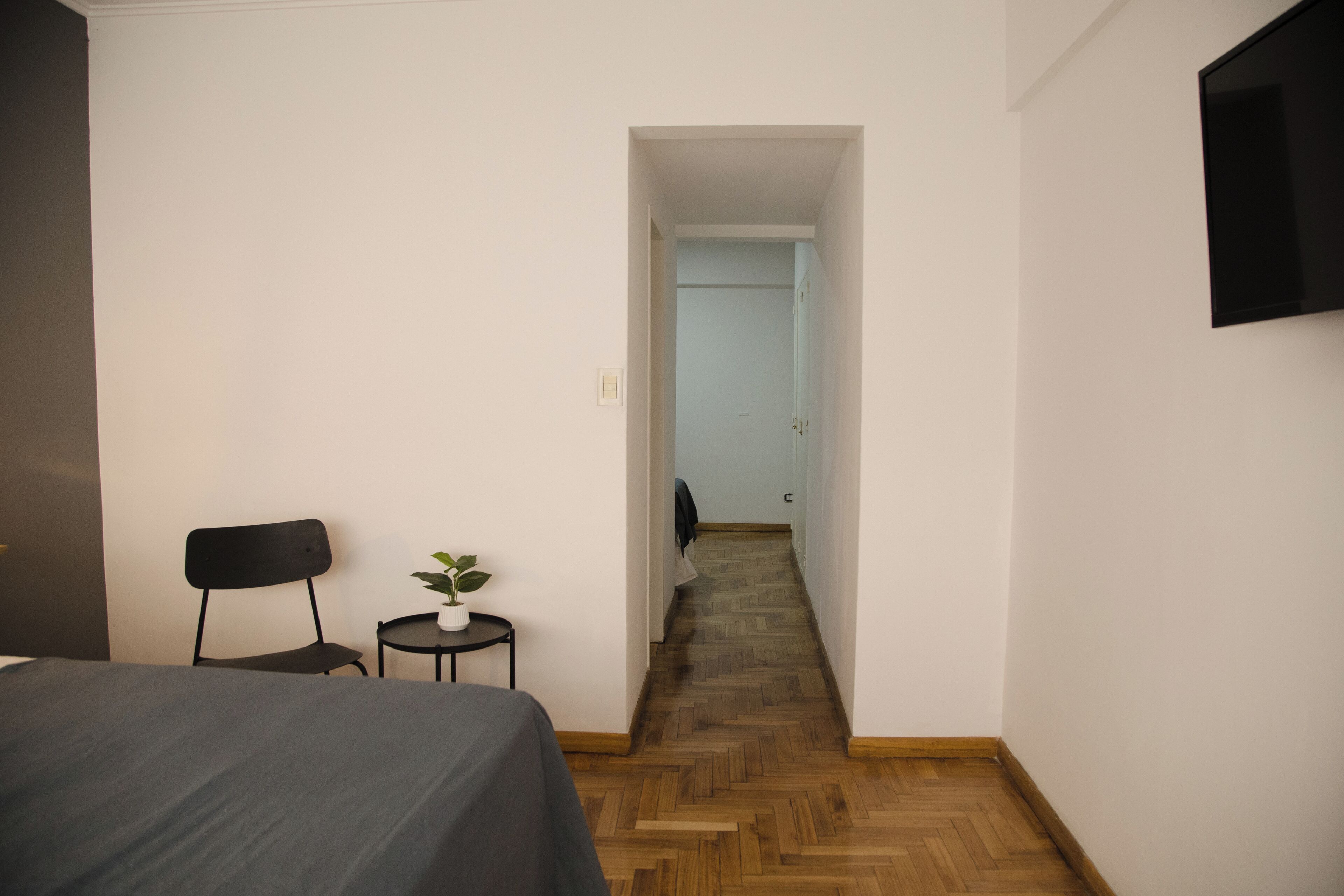 Una habitación de hotel con una cama, una mesita con una planta, una silla y un televisor en la pared.