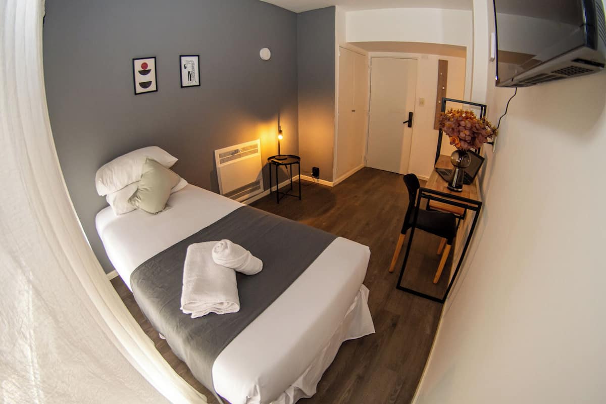Une chambre d’hôtel équipée d’un lit, d’une table de chevet, d’une chaise, d’un bureau avec un ordinateur portable et d’un téléviseur fixé au mur.