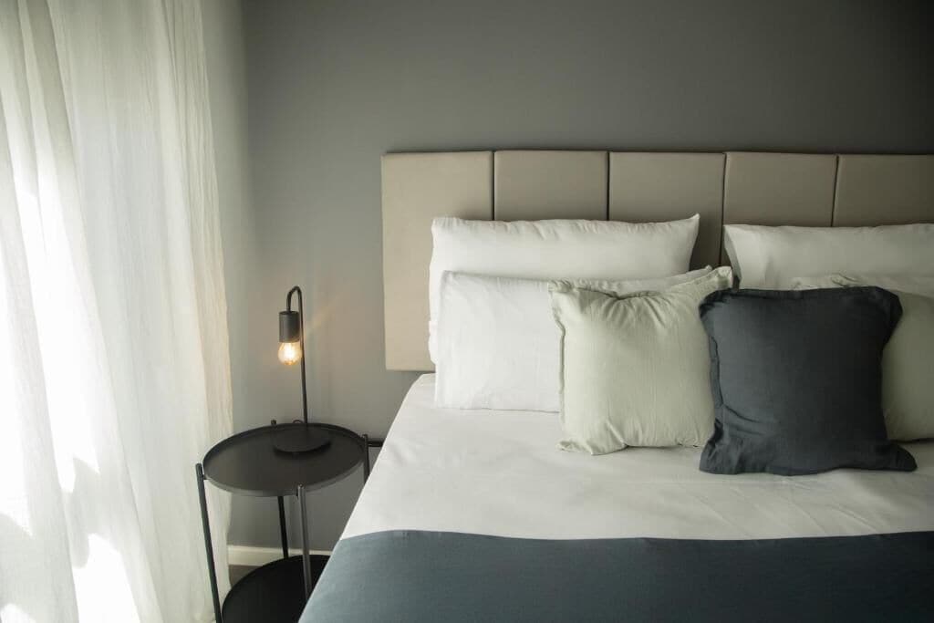 A neatly made bed with a headboard, a bedside lamp, and a small round table.