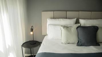 A neatly made bed with a headboard, a bedside lamp, and a small round table.
