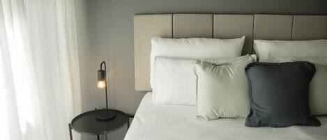 A neatly made bed with a headboard, a bedside lamp, and a small round table.