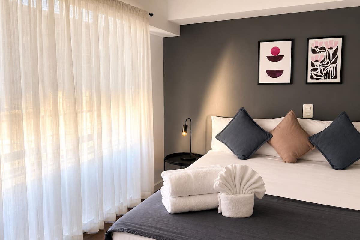 Une chambre à coucher avec un lit, des oreillers, une lampe de chevet et des œuvres d’art accrochées au mur.