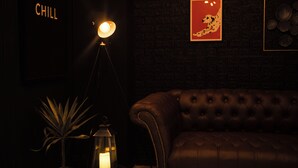 Una habitación oscura con un sofá de cuero, una lámpara de pared, un cuadro enmarcado y un letrero que dice "CHILL".