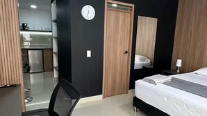 Una habitación de hotel moderna con cama, escritorio, silla, reloj y puerta.