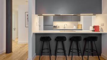 A modern kitchen with a white countertop, grey cabinets, and a red coffee machine.