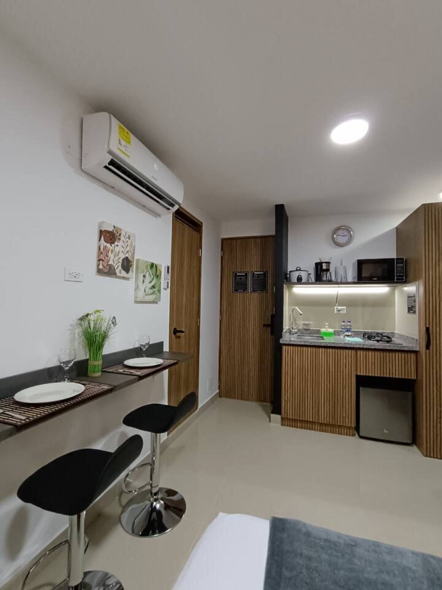 A modern kitchen with a microwave, sink, and cabinets. There are two bar stools and a small dining table with plates.