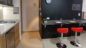 Een moderne keuken met een gasfornuis, magnetron en een zwart aanrecht. Er staan twee rode barkrukken bij en een klok hangt aan de muur.