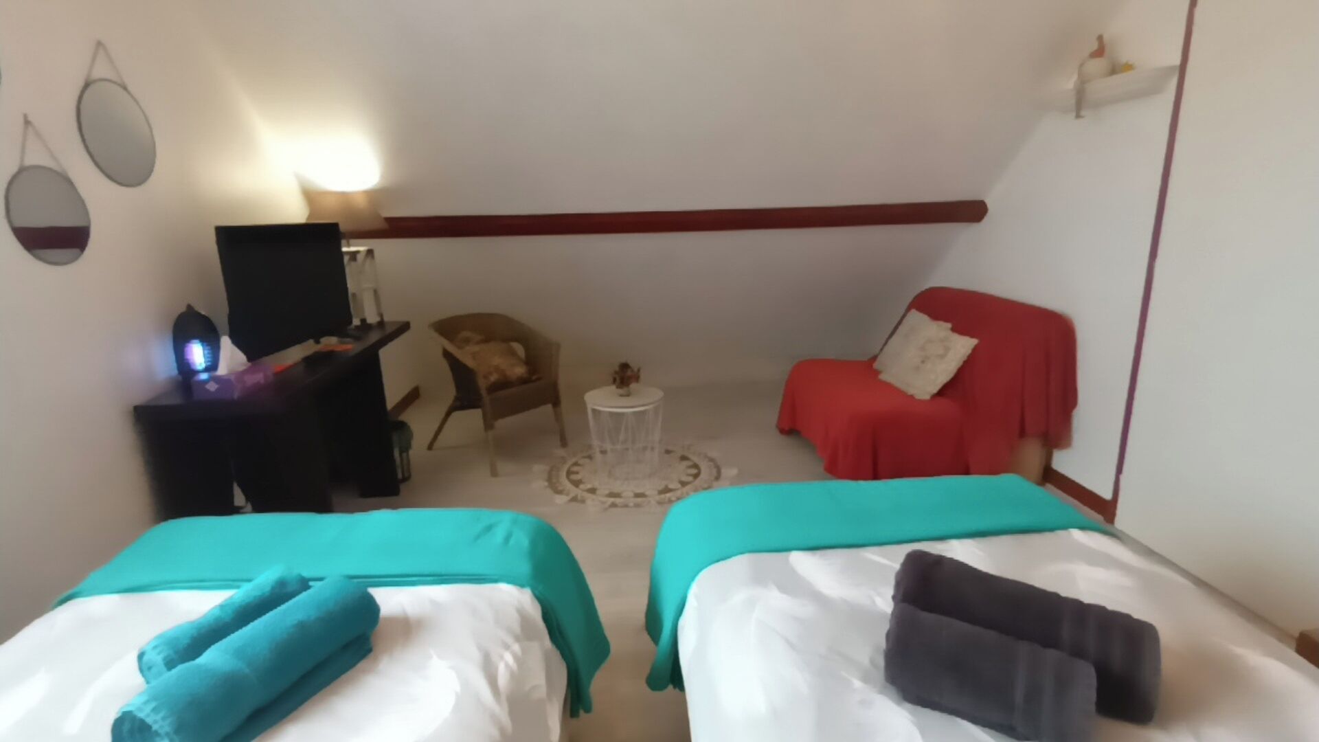 A room with two beds, a desk, a chair, a small table, and a red chair.