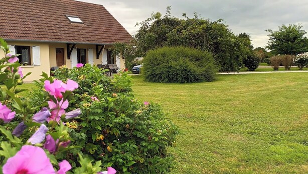 A house with a brown roof and beige walls, surrounded by a well-maintained lawn and various bushes. - Guest rooms upstairs.  Breakfast included.  (Saillenard)