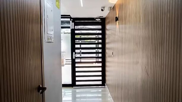Un pasillo moderno con piso brillante, paneles de madera en las paredes y una puerta con marco negro.
