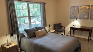 A bedroom with a bed, a chair, a desk, and a window with curtains.