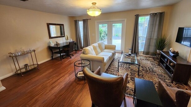 A spacious living room with a beige sofa, a brown armchair, a coffee table, and a TV on a wooden cabinet.
