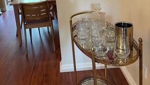 A dining area with a wooden table and chairs, a glassware tray, and a painting on the wall.