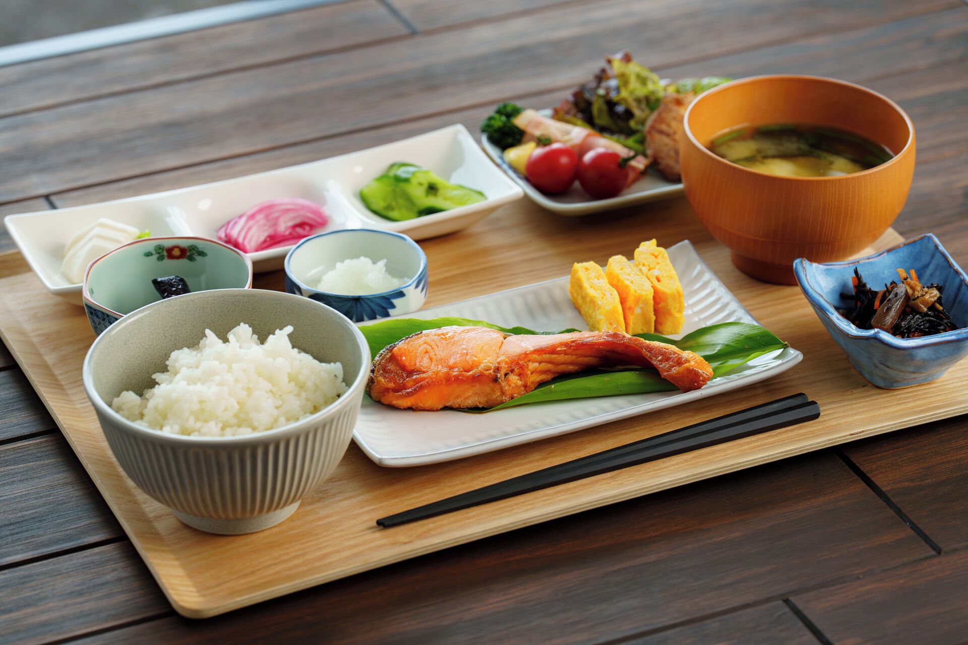 A wooden tray with various Japanese dishes including rice, fish, vegetables, and a bowl of soup.