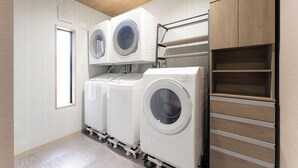 A laundry room with two stacked front-loading washing machines, a drying rack, and a wooden cabinet with shelves. - CS RESORT (Miyakejima)