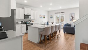 Una cocina moderna con armarios blancos, una isla central con taburetes y una zona de comedor con sofá azul.