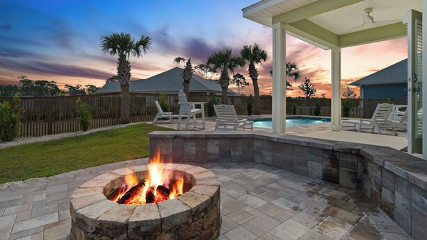 Un patio trasero con un pozo de fuego de piedra, un área de patio techada con sillones de descanso y una piscina.