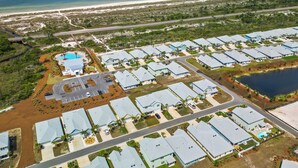 Vista aérea de una zona residencial costera con varias casas independientes, una piscina y una playa.