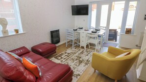 Ein Wohnzimmer mit einem roten Ledersofa, einem gelben Sessel, einem Esstisch mit Stühlen, einem Flachbildfernseher und einem Kamin.