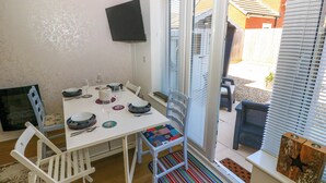 Ein Essbereich mit einem weißen Tisch, gedeckt für vier Personen, umgeben von weißen Stühlen. An der Wand über dem Tisch ist ein Fernseher angebracht.