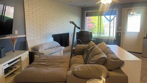 A living room with a white brick wall, a large window, a ceiling fan, and a flat-screen TV. - Workspace near Microsoft, Meta, Lumen Field and T-Mobile Park (Bellevue)